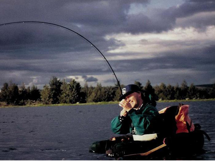 Man in float tube with a large fish on the line.